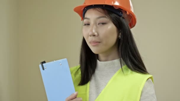 Asian woman builder in protective clothing. A young woman is holding a folder with documents and smiling. — Wideo stockowe