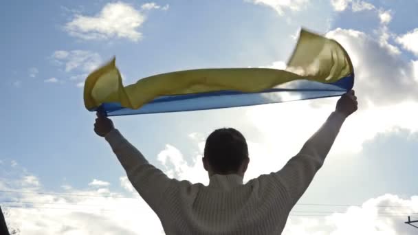 Mulher segura uma bandeira acenando da Ucrânia contra um céu azul. — Vídeo de Stock