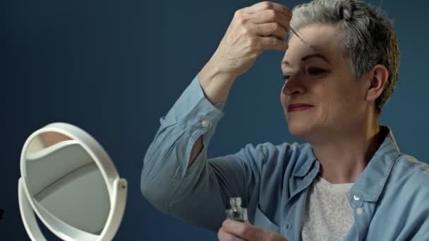 Schöne ältere Frau wendet ein feuchtigkeitsspendendes und nährendes Kosmetikprodukt für die Hautpflege an. — Stockvideo