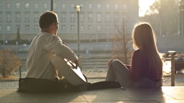 Rendez-vous romantique sur le front de mer. Deux amoureux sont assis sur le remblai de la ville. Il joue de la guitare pour la fille.. — Video