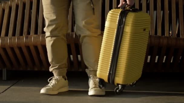 一个人的腿，他在车站的长椅上坐下来等着他的航班。旁边是一个黄色的手提箱. — 图库视频影像