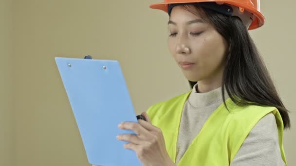 Asian builder woman, wearing protective clothing and a helmet, is writing down something. — Vídeo de Stock