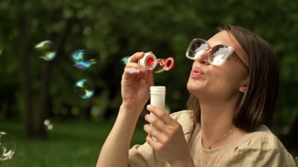 Close-up. Beautiful young woman blowing rainbow soap bubbles. A childs hand catches them. — Wideo stockowe