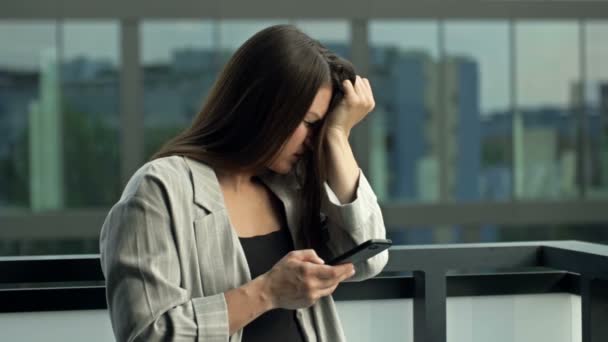 Jonge vrouw met een smartphone in haar handen. Haar gezicht drukt emoties uit van verdriet, angst en verwarring.. — Stockvideo