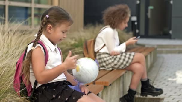 Twee Schoolmeisjes Van Verschillende Leeftijden Zitten Een Bankje Het Schoolplein — Stockvideo