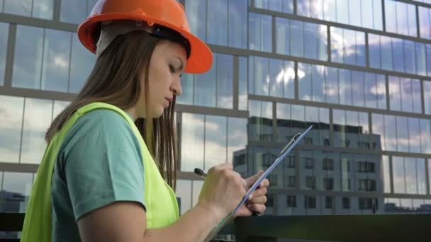 Young Female Builder Signal Vest Helmet Writes Something Backdrop Building — 图库视频影像