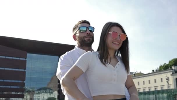 愛好家のカップルは ヨーロッパの都市の美しい広場を通って電動スクーターに乗っています サングラスの男と女は喜んで笑顔 — ストック動画