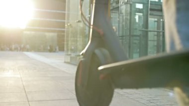Sırt çantalı bir adam şehir caddesinde katlanmış bir scooter taşıyor. Arkadan bak. HD.