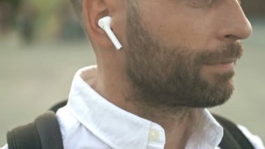 Yakın plan. Kulağında beyaz kablosuz kulaklık olan orta yaşlı bir adamın profili. HD.
