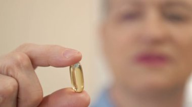 Elinde balık yağı kapsülü tutan kadın. Omega-3 içeren bir beslenme takviyesi olarak balık yağı kapsülleri ve sağlık hizmetleri için A vitamini yüksektir. HD.