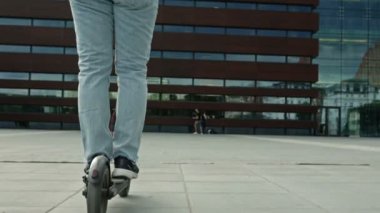 Man with a backpack and in a protective helmet rides an electric scooter through the city square. The concept of convenient and environmentally friendly individual urban transport. 4K.