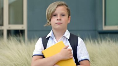 Portrait of a cheerful little schoolboy standing with textbooks in her hands in the school yard. Back to school. HD.