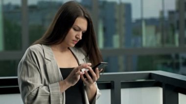 Young woman stands on the office balcony with a smartphone in her hands and surfs the Internet. HD.