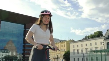 Cheerful young woman rides an electric scooter through a beautiful town square. HD.