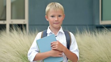 Portrait of a cheerful little schoolboy standing with textbooks in her hands in the school yard. Back to school. HD.