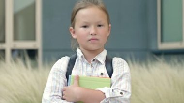 Portrait of a cheerful little schoolgirl standing with textbooks in her hands in the school yard. Back to school. HD.