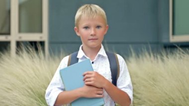 Portrait of a cheerful little schoolboy standing with textbooks in her hands in the school yard. Back to school. HD.