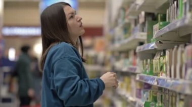 A young woman shopper chooses the right product on a shelf in a supermarket. HD.