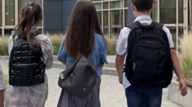 Dört birinci sınıf öğrencisi, iki erkek ve iki kız, okul binasına yaklaşın. Okula dönelim. HD.