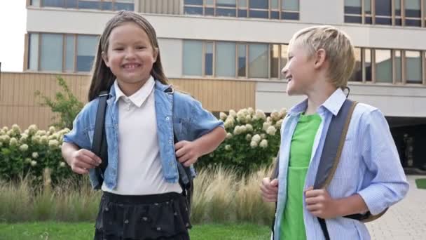 2人の小さなクラスメート 男の子と女の子は 良い気分で学校の庭を歩いている 学校の友情 — ストック動画