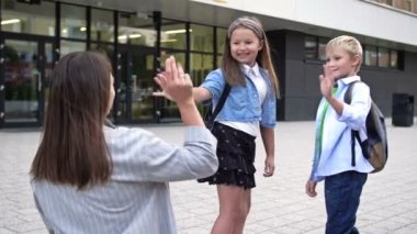 Annem çocukları okula götürüyor. Kadın el sallıyor, çocuklar okul bahçesinde koşuşturuyor. HD.