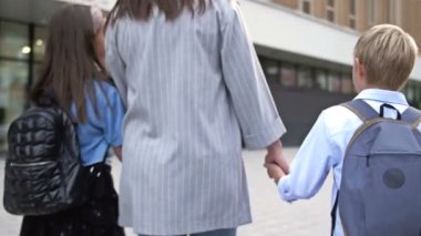 Genç bir kadın, 8-9 yaşlarındaki bir çocukla bir kızı okula götürüyor. Anne çocukları ellerinden tutuyordu. 4K.