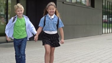 Okul arkadaşlığı. Bir erkek ve bir kız, ilkokul öğrencileri, el ele tutuşarak okul binasından çıkıyorlar. 4K.
