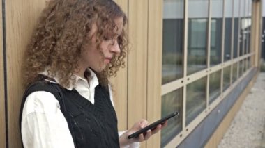 Elinde telefon olan liseli kız duvara dayanıyor. 4K.