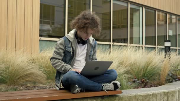Krøllet Teenager Sidder Med Bærbar Computer Bænk Baggrund Kontorbygning Fyren – Stock-video