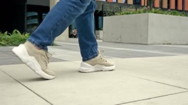 Spor ayakkabılı kadın bacakları ve kaldırımda açık renkli fayanslarla döşenmiş kot pantolonlar. Sonbaharın başında şehir caddesi. 4K.