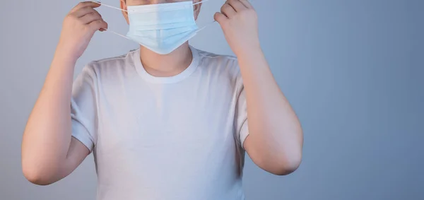 Молодой человек надевает противовирусную защитную маску, чтобы защитить других от коронавирусной инфекции COVID-19 и SARS cov 2. На сером фоне копирования пространства — стоковое фото