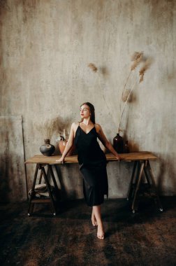 Bir sanat stüdyosunun masasının yanında siyah elbiseli uzun boylu esmer bir kız..