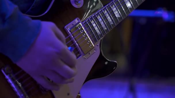大ホールステージでエレキギターを弾く男性ギタリストの手のクローズアップ — ストック動画