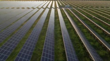 İnsansız hava aracı, güneşli bir yaz akşamında güneş panellerinin üzerinden uçar. Güneş pili santralleri, yeşil çimenler. Görüntü 4k.