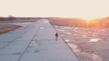 Camera rotates around bearded man walking along concrete road for planes at bright winter sunset