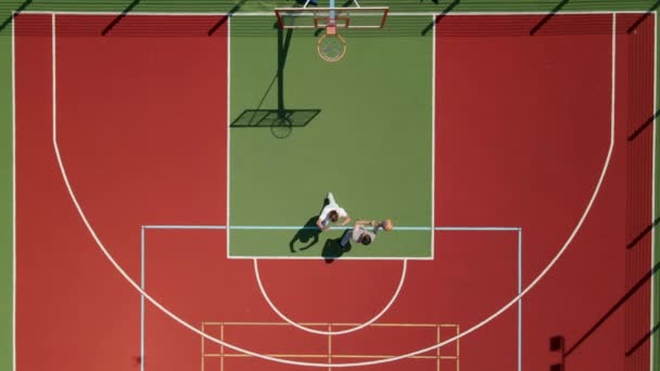 Vista aérea de dos jóvenes amigos jugando baloncesto en la cancha al aire libre. — Vídeo de stock