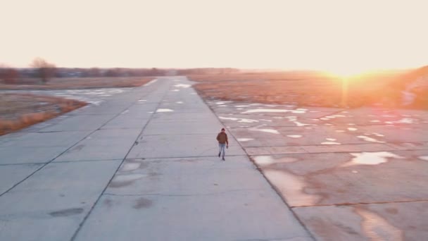 Camera rotates around bearded man walking along concrete road for planes at bright winter sunset — Vídeos de Stock