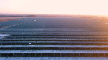 Kışın erken saatlerinde güneş batımında güneş çiftliğindeki büyük güneş panellerinin insansız hava aracı görüntüsü. Güneş pili santralleri