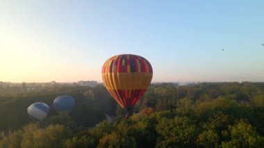 Ukrayna 'nın Kiev bölgesinde yaz gündoğumunda küçük Avrupa şehrinde yeşil parkın üzerinde uçan renkli sıcak hava balonlarının insansız hava aracı görüntüsü