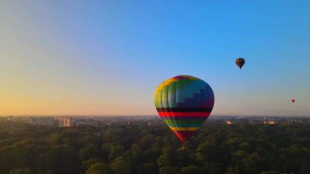 夏の日没、キエフ地域、ウクライナで小さなヨーロッパの都市で緑の公園を飛んでカラフルな熱気球の空中ドローンのHDRビュー — ストック動画