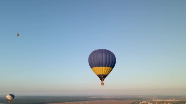 Luftaufnahme eines bunten Heißluftballons mit ukrainischer Flagge, der bei Sonnenaufgang über einem grünen Park in einer kleinen europäischen Stadt fliegt, Region Kiew, Ukraine — Stockvideo