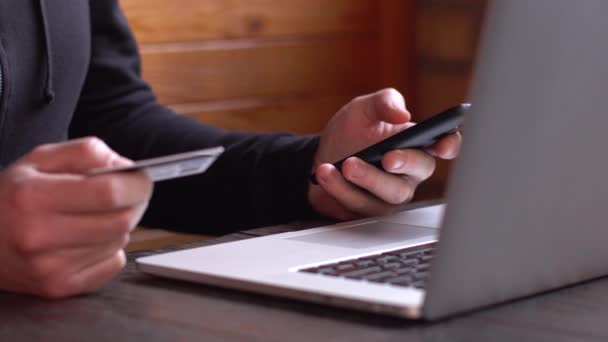 Zakenman in een zwarte hoodie doet online betaling met creditcard en smartphone, online winkelen — Stockvideo
