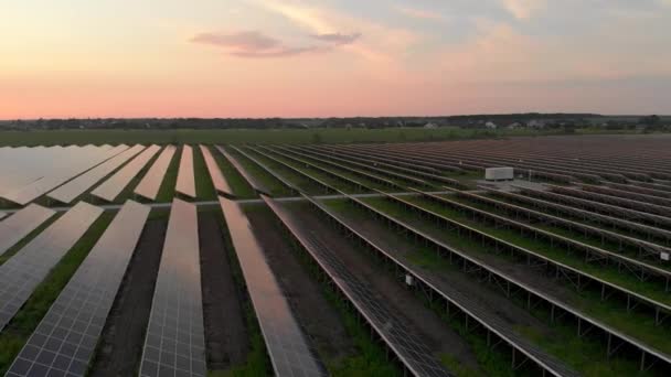 Flygdrönare utsikt över stora solpaneler på en solgård på molnig sommarkväll. Solcellskraftverk, grönt gräs. Videofilm 4k. — Stockvideo