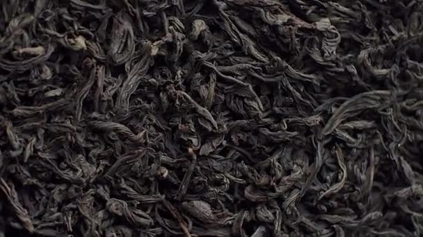 Fondo para un café o restaurante, té negro de hojas sueltas espolvoreado en un plato y girando de cerca, publicidad de té — Vídeo de stock
