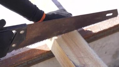 Close up of professional man carpenter using hand saw to cutting wood on workbench at workshop. Carpentry, craftsmanship and handwork concept