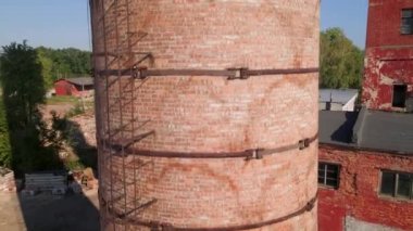 Old brick pipe on empty plant. Abandoned factory with many ruined buildings. Deserted industrial territory. Close up aerial 4k shot.