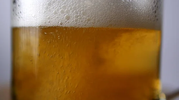 Close-up shot of light beer is poured into a beer glass with a handle, a lot of bubbles and foam. 4k colorcorrected footage