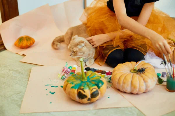快乐的小女孩在家里用猫装饰南瓜 小女孩在橙色万圣节前夕用南瓜画着脸 假日装饰概念 — 图库照片
