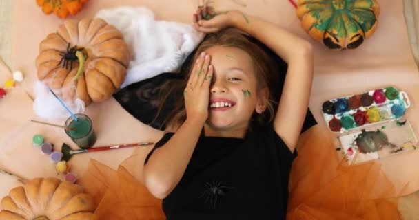 描かれたカボチャのハロウィンの間の床に横たわっている笑顔の女の子のトップビュー パーティーのための装飾 手をペイント 顔を作る — ストック動画