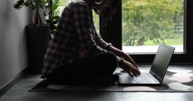 Serbest çalışan bir kadın dizüstü bilgisayarda oturuyor, büyük pencerelerin yanında yerde oturuyor, içeriği olan bir kadın not defterine bakıyor, çalışıyor, evden çalışıyor..